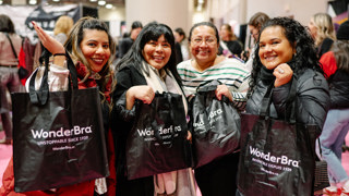 Quatre participantes à un salon tiennent des sacs promotionnels dans un espace d’exposition achalandé.