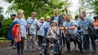 Groupe de personnes marchant ensemble dans un parc, dont une personne en fauteuil roulant, lors d’un événement de mobilisation.