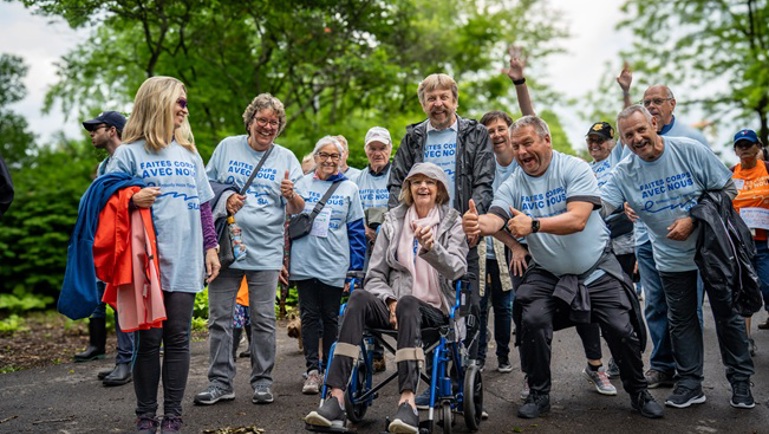 Groupe de personnes marchant ensemble dans un parc, dont une personne en fauteuil roulant, lors d’un événement de mobilisation.