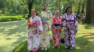 Quatre personnes en kimonos colorés posent dans un parc verdoyant, près d’un étang. 