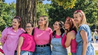 Six femmes posent ensemble dans un parc ensoleillé devant un grand arbre. Elles portent des vêtements dans des tons de rose et de bleu denim, avec des chaussures roses assorties. Elles sourient et regardent dans la même direction, créant une ambiance conviviale et festive.
